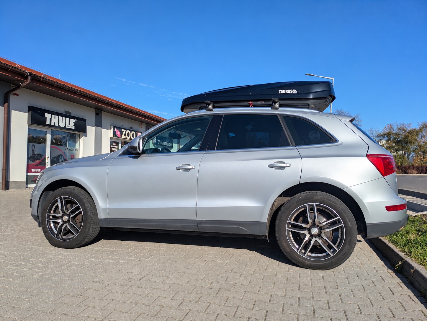Srebrne Audi Q5 z boxem Taurus Strike 440 i bagażnikiem bazowym Aguri Runner R2 C/D ? widok z boku
